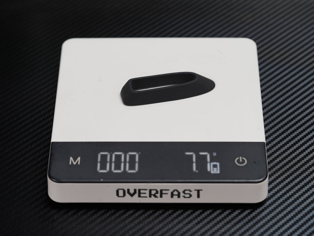 A white digital pocket scale with a black display screen and a black handle on top, resting on a black carbon fiber textured surface. The brand name 'OVERFAST' is clearly visible on the front.