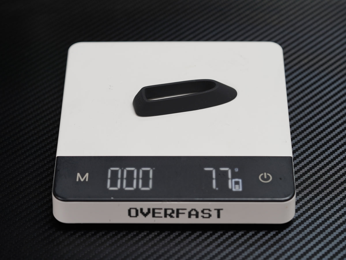 A white digital pocket scale with a black display screen and a black handle on top, resting on a black carbon fiber textured surface. The brand name 'OVERFAST' is clearly visible on the front.