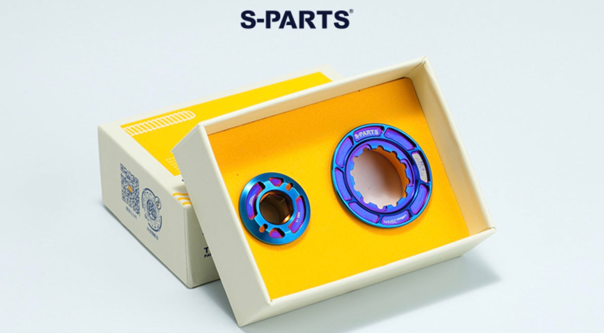Two metallic ball bearings with blue and purple accents displayed inside an open yellow and beige S-PARTS box, with the S-PARTS logo printed above on a clean white background.